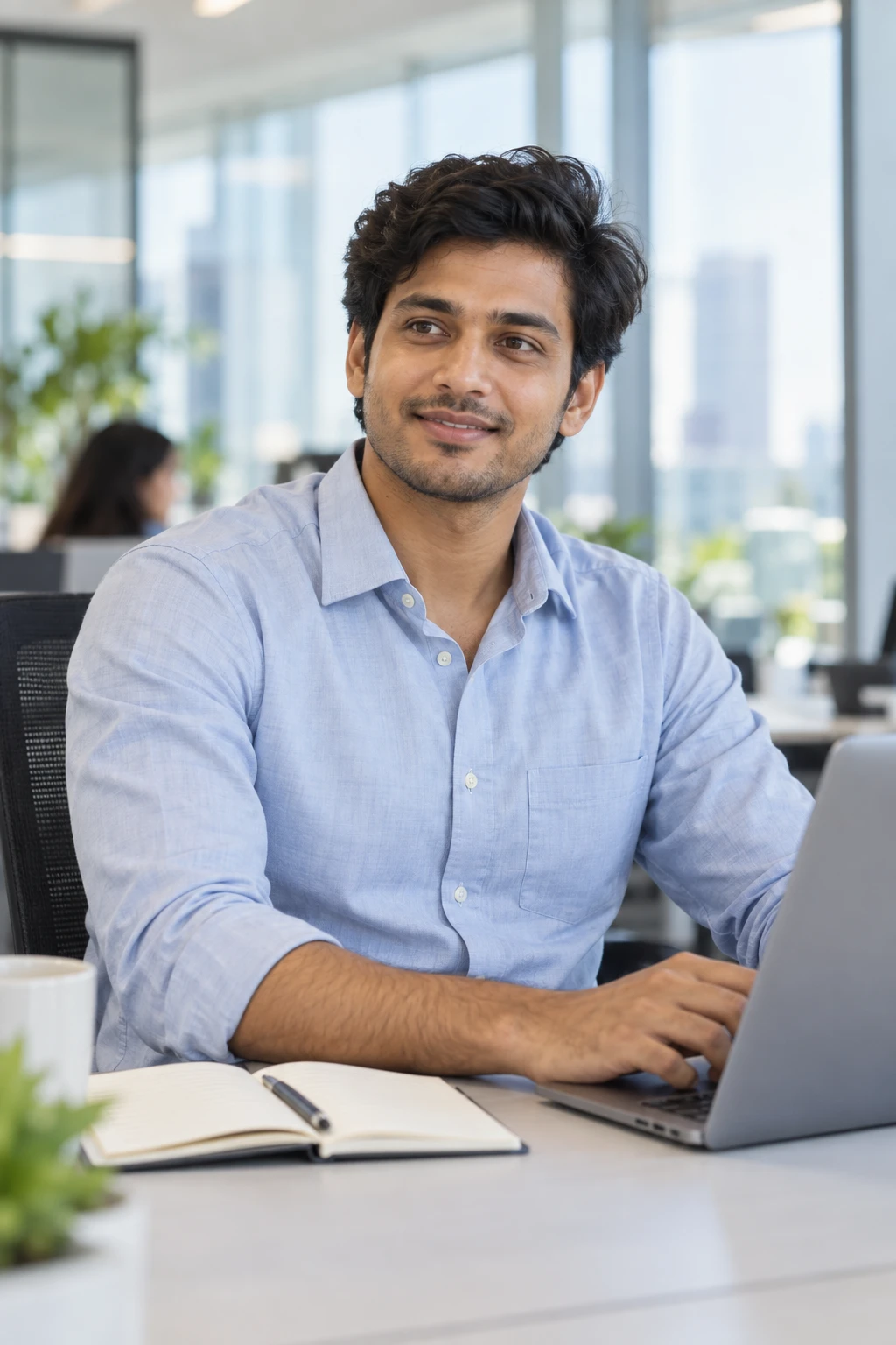 An early-career Indian professional working confidently at a laptop in a contemporary office