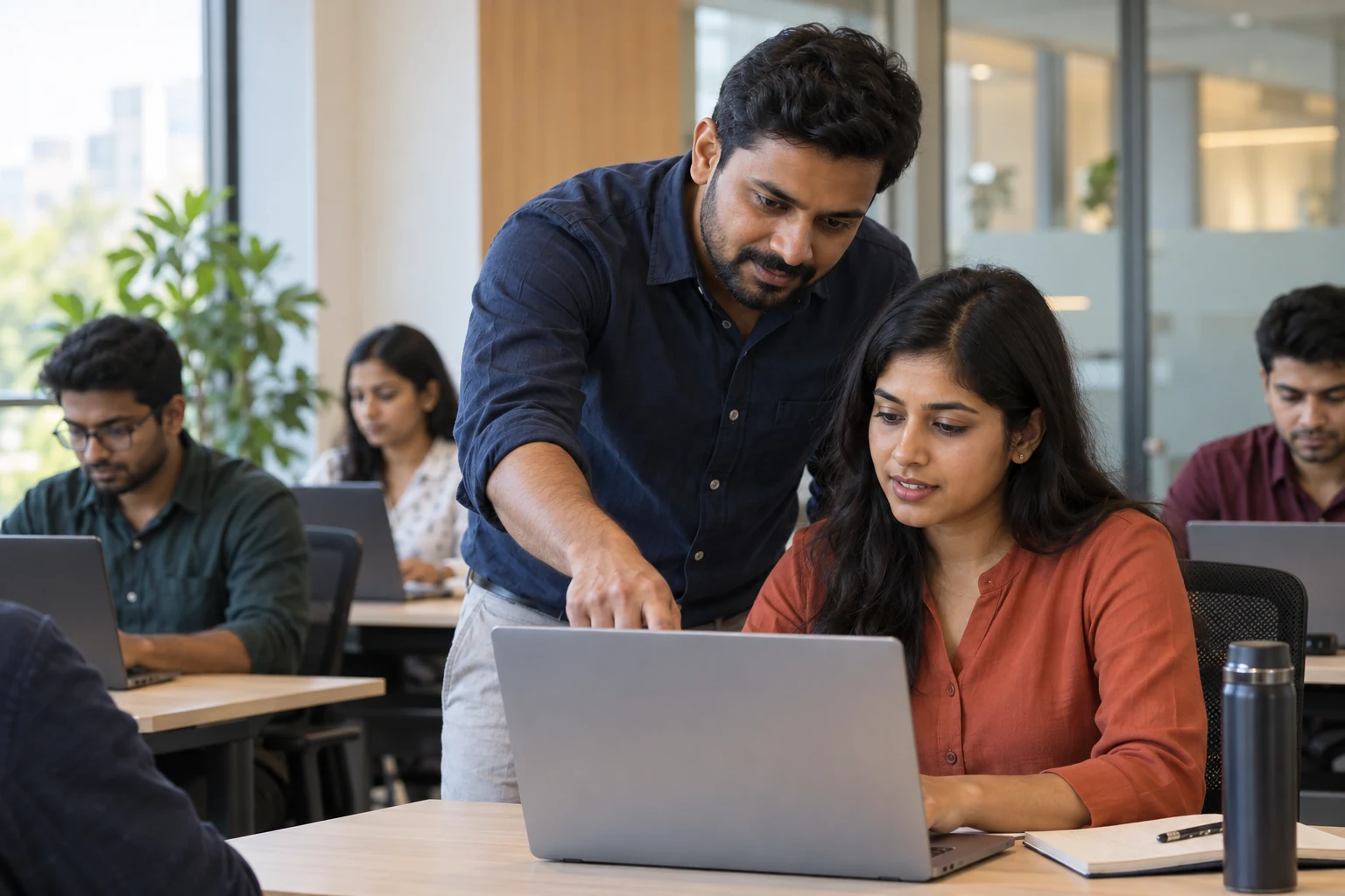 A technical mentor guiding a software trainee through a practical laptop exercise